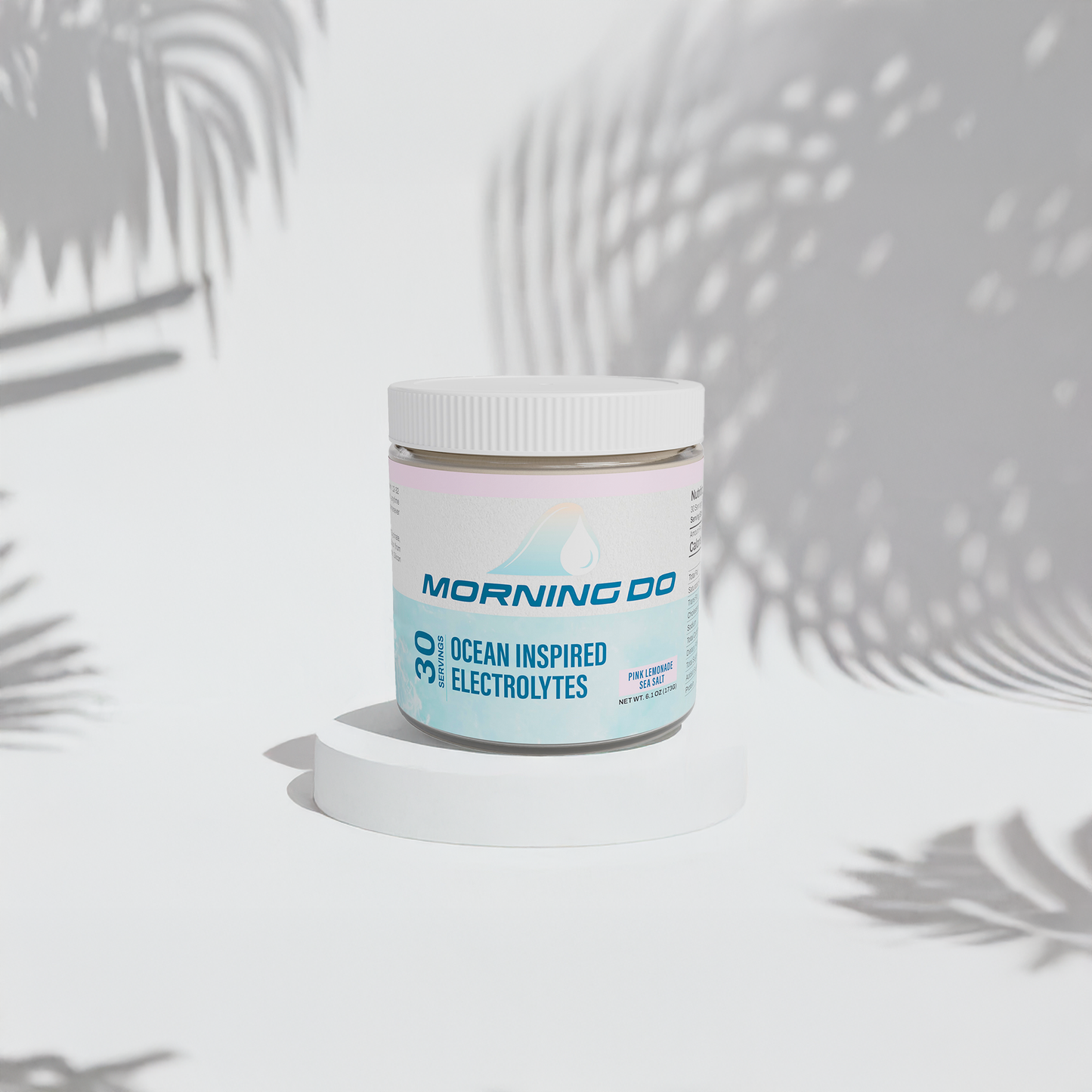 A container of Morning Do Hydration powder with the flavor Pink Lemonade, placed on a surface with a shadow of a plant leaf falling over it.